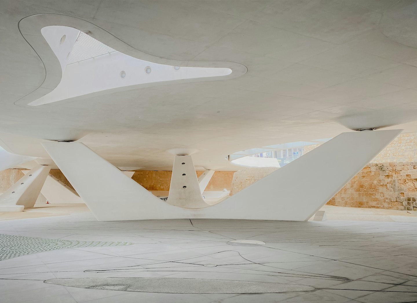 Curved concrete architectural supports stand against a stone wall.