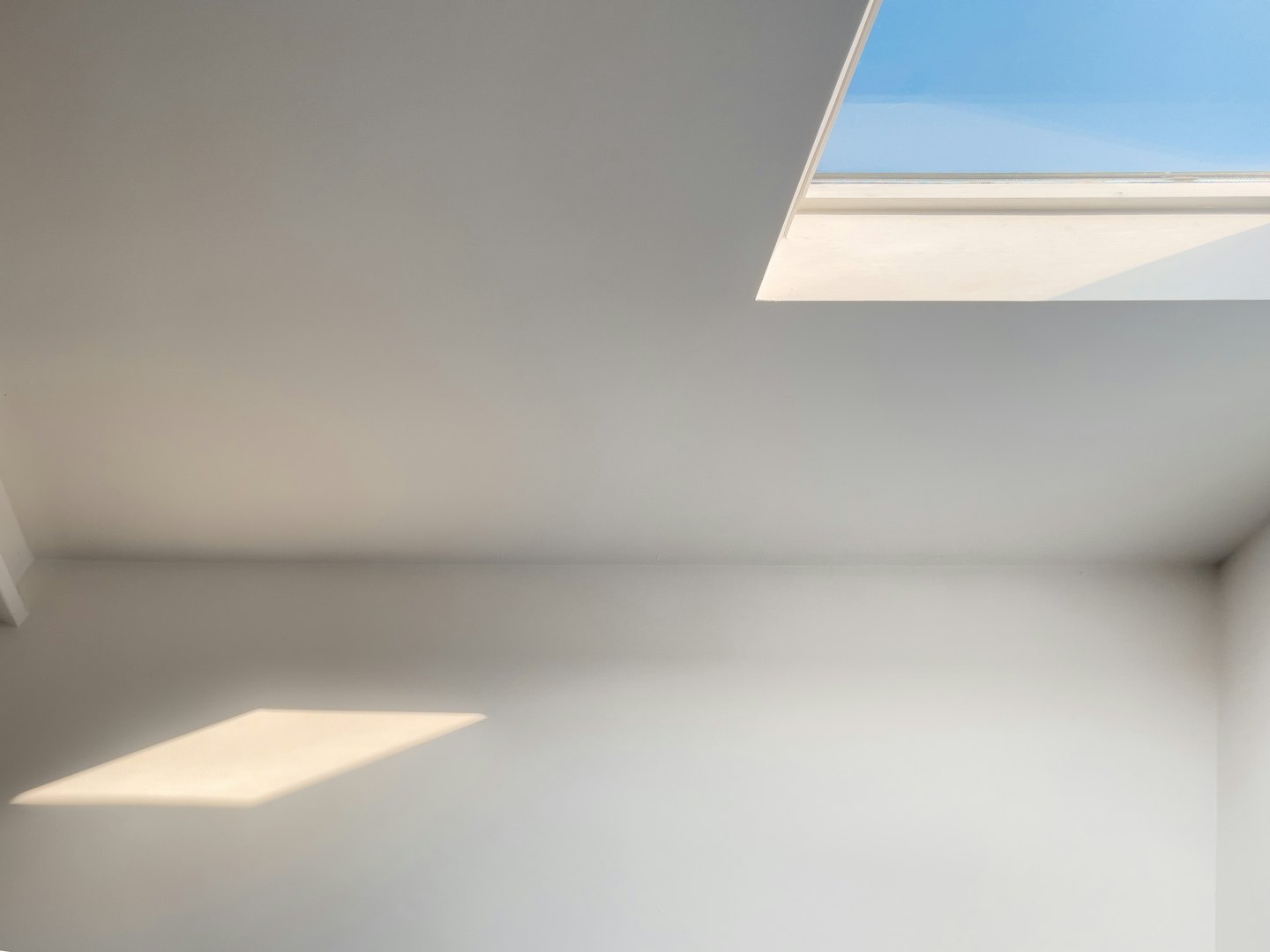 Sunlight streams into a minimalist white room through a skylight.