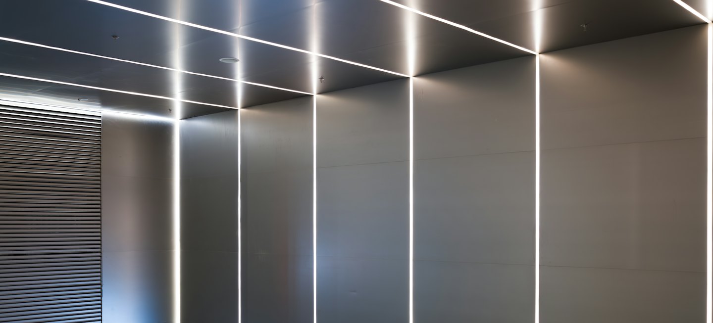 Linear LED lights illuminate grey panels in a minimalist room.